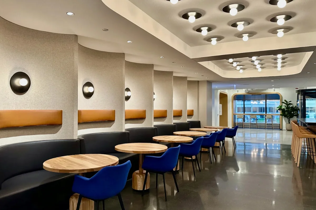نورپردازی سقف و دیوارهای شرکت هواپیمایی با میزهای چوبی گرد و صندلی‌های آبی در محیط