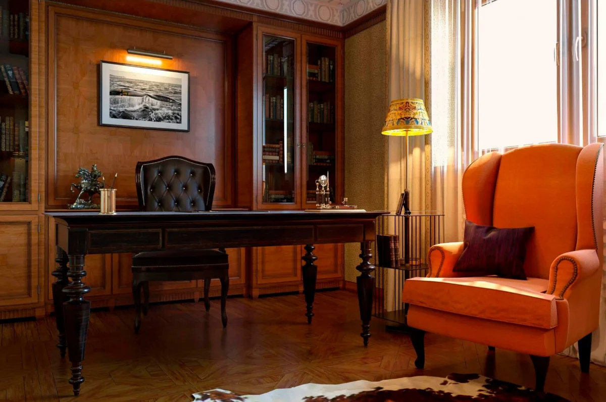 اتاق‌کار لوکس با میز و صندلی قهوه‌ای و مبل نارنجی و دیوارهای چوبی و یک آباژور زرد