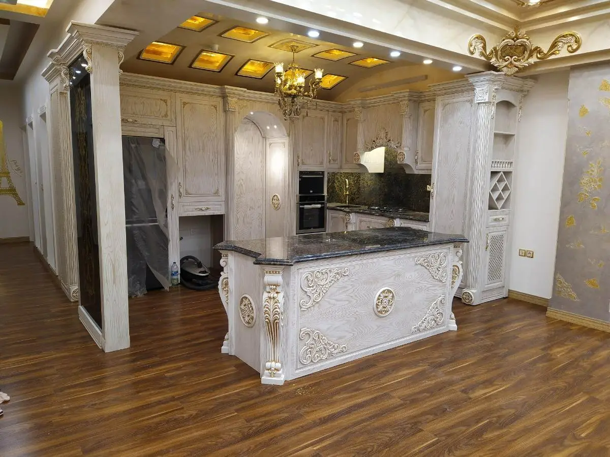  کابینت کلاسیک سفید با منبت کاری‌های طلایی در آشپزخانه با کفپوش طرح چوب