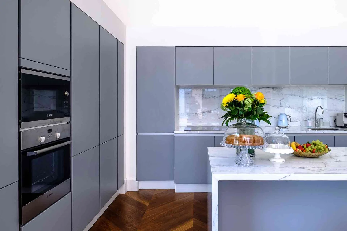 آشپزخانه مدرن با دیوار سفید و کابینت طوسی با صفحه بین کابینتی طرح ماربل