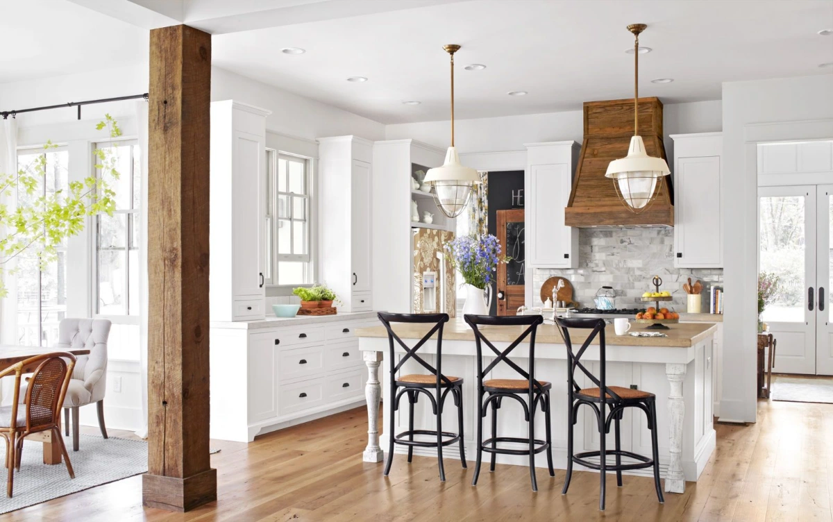 ستون چوب طبیعی وسط آشپزخانه با کاور هود چوبی قهوه‌ای و کابینت‌های سفید