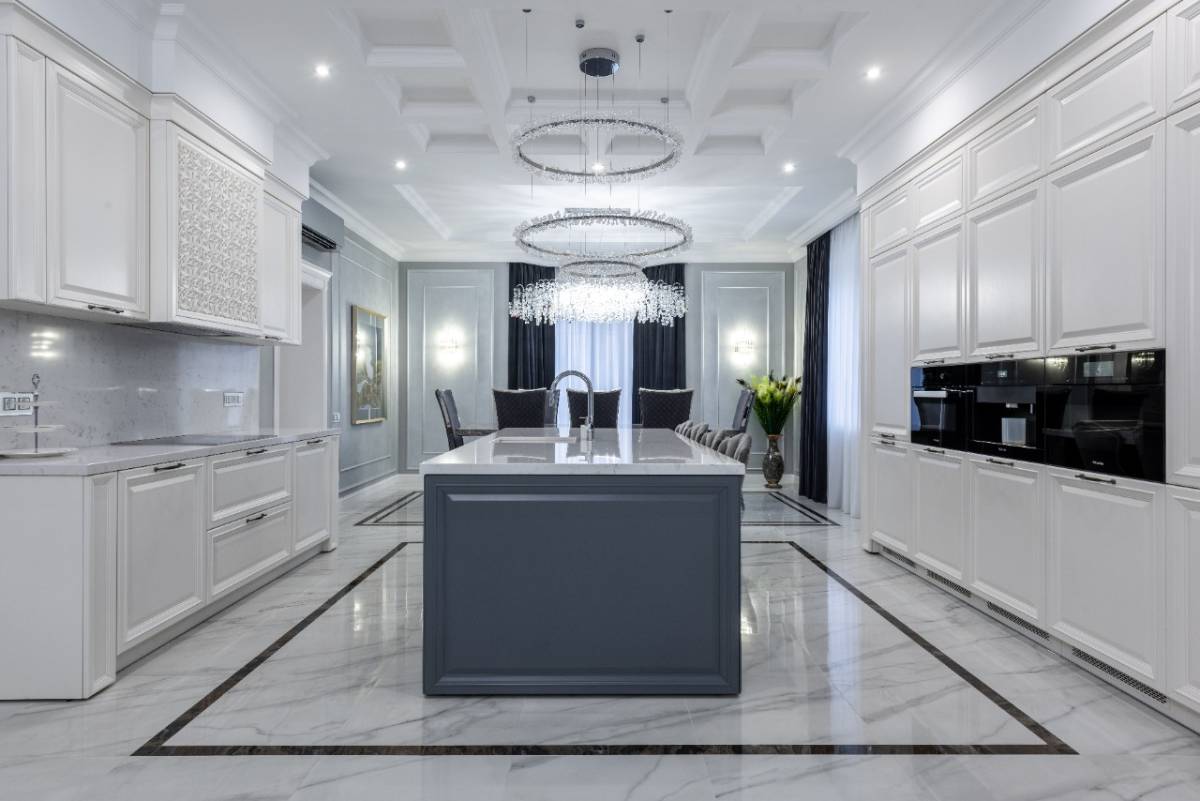 دکوراسیون آشپزخانه نئوکلاسیک با کابینت سفید و جزیره طوسی و لوستر کریستالی آویز سه طبقه