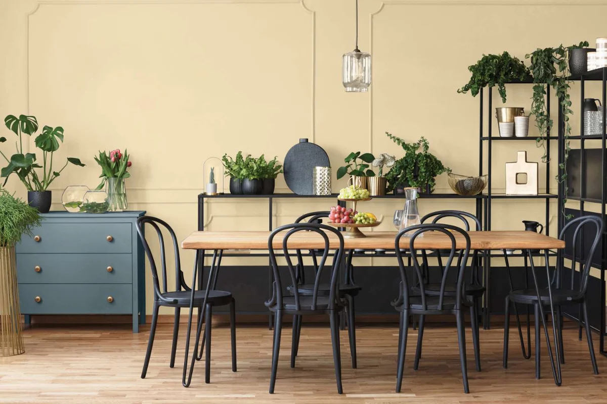 ناهارخوری خانه با دیوار زرد نخودی و میز چوبی با صندلی‌های ‌مشکی