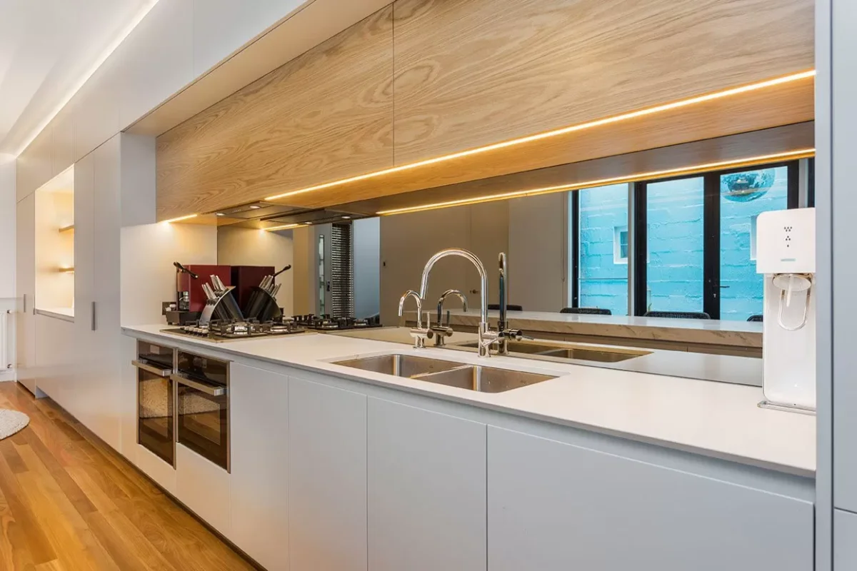 آشپزخانه مدرن با کابینت‌های سفید و قهوه‌ای و نورپردازی مخفی در زیر و بالای کابینت‌ها