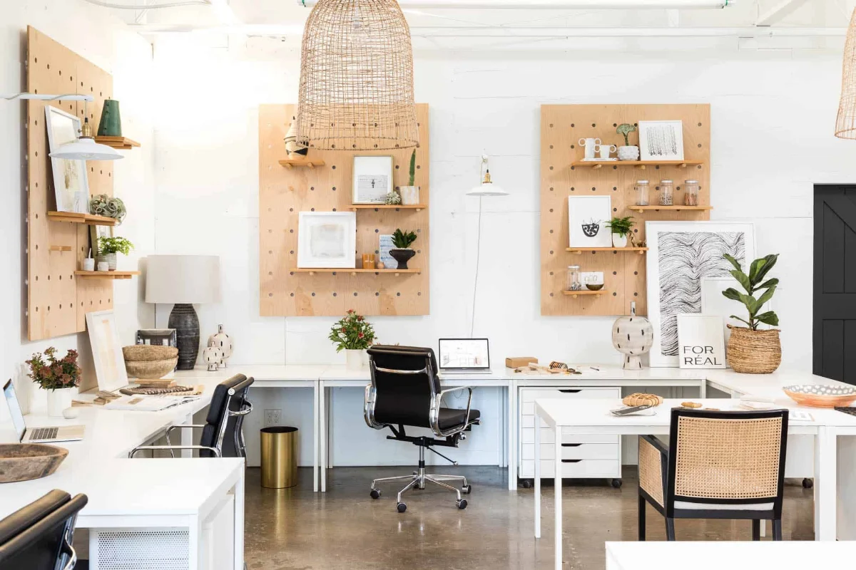 دفترکار با میزهای سفید و صندلی‌های کرمی و مشکی و قفسه دیواری چوبی