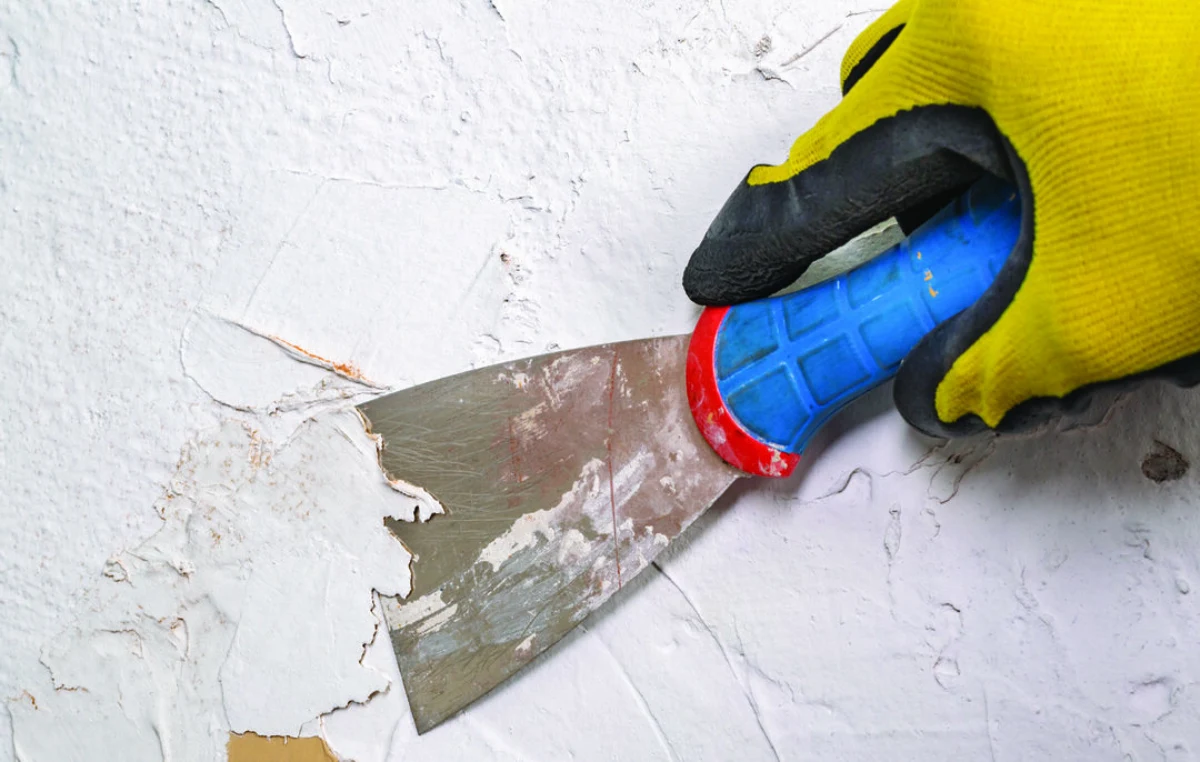 تراشیدن رنگ دیوار خانه با کاردک برای ترمیم پوسته شدن رنگ دیوار