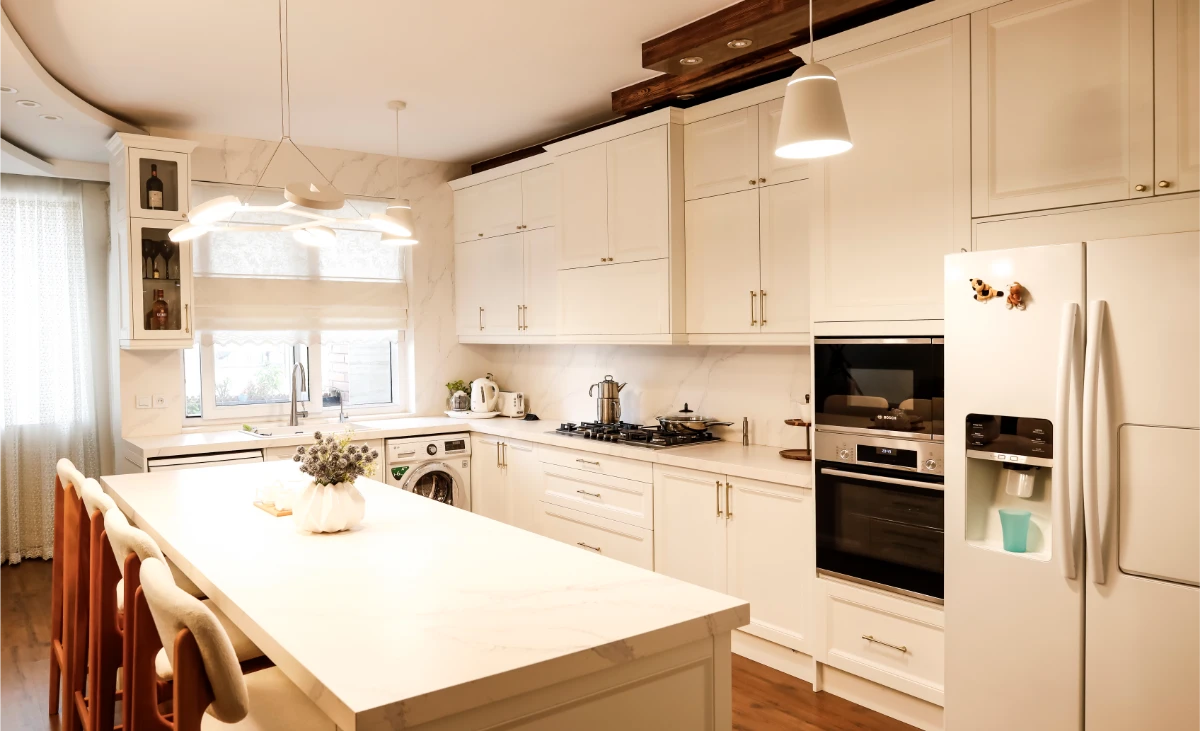 آشپزخانه با کابینت‌های نئوکلاسیک سفید و دستگیره فلزی و اپن جزیره