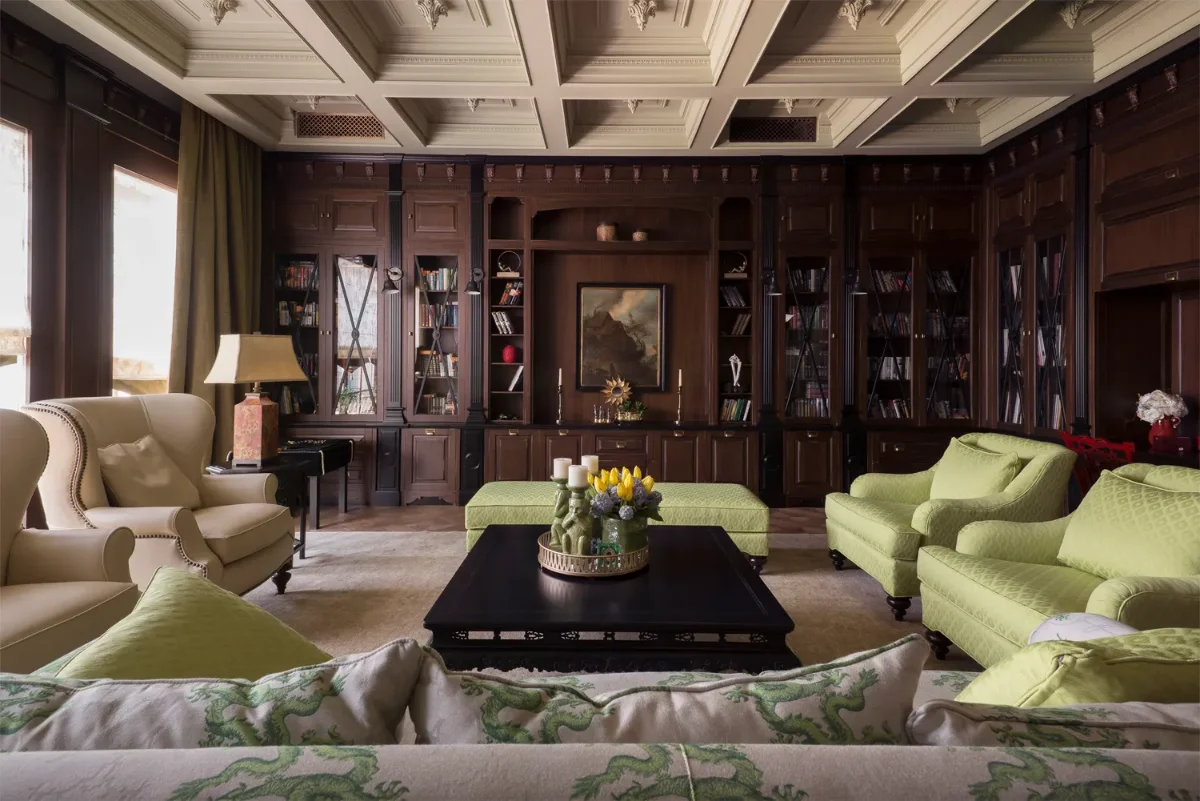 اتاق بایگانی کلاسیک با کتابخانه‌ی چوبی تیره و مبلمان کرمی و سبز
