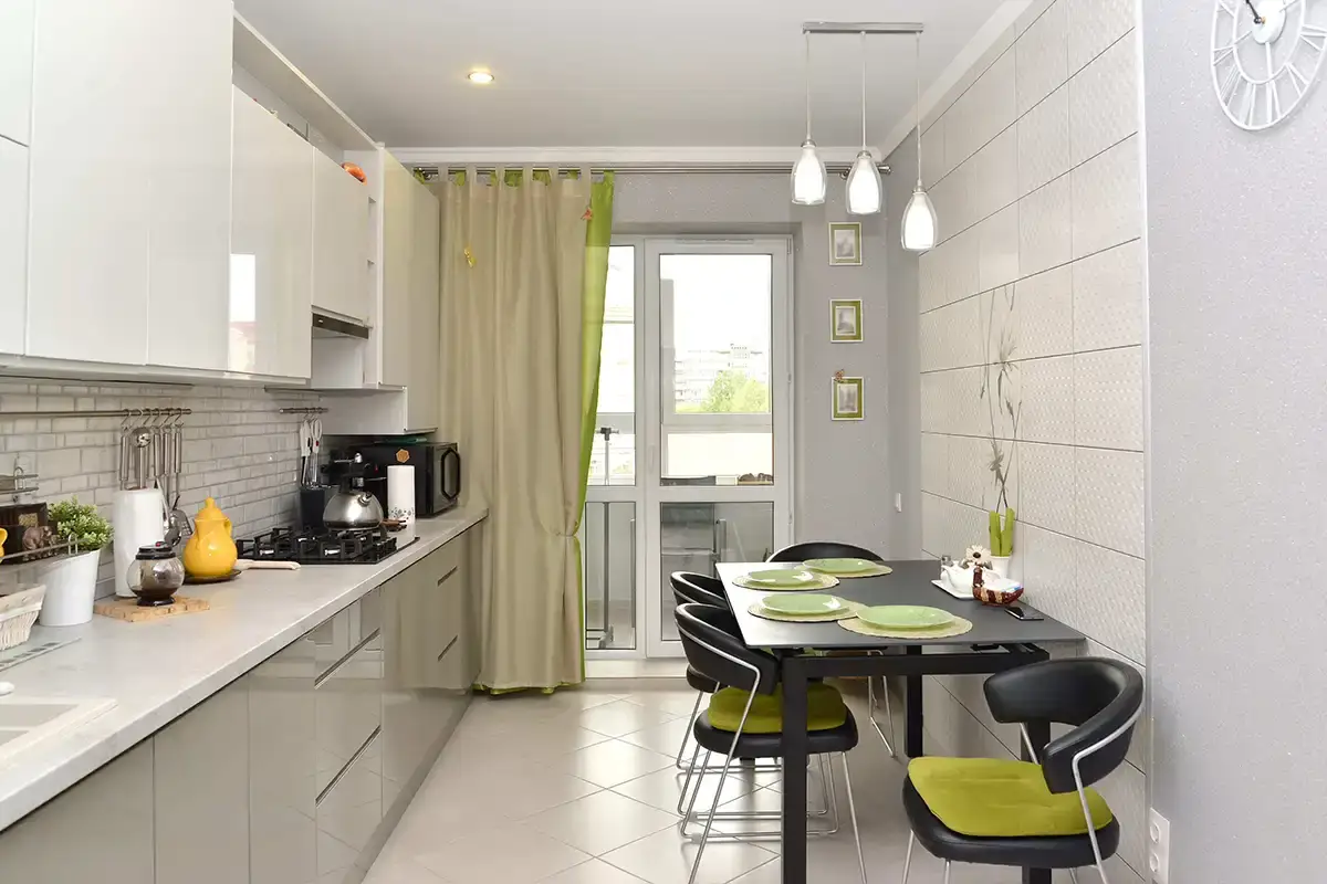 آشپزخانه کوچک با کابینت‌های روشن و میز ناهارخوری مشکی و سبز که صندلی‌هایی مینیمال و کم‌جا دارد